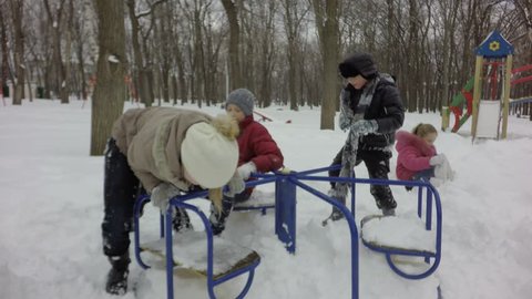 Little children have fun in the winter. Happy kids ride on the carousel. Children play on the playground. Winter sunny day. It's snowing, it's cold. 