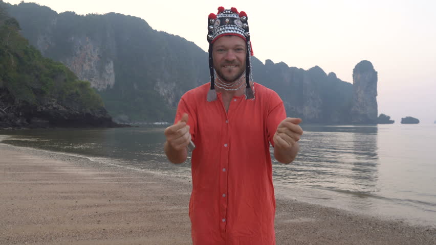 Freaky Caucasian Man in Traditional Thai Womens Hat Playing on his Harp at the Morning Twilight on the Coastline of Beautiful Tropical Rocky Cliff Lagoon in Krabi, Thailand.