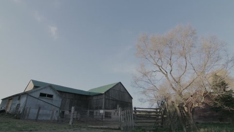 Wide shot time-lapse of barn on a farm with wispy clouds from day to night.