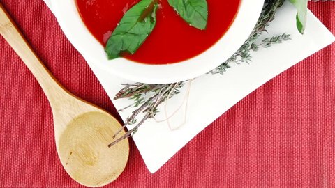 cold fresh diet tomato soup with basil thyme and dry pepper in big bowl over red mat on wood table ready to eat 1920x1080 intro motion slow hidef hd