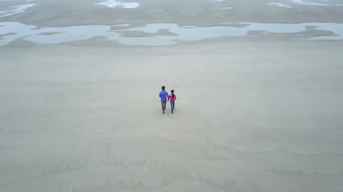 This is a footage of a father and daughter holding hands walking on the huge beach