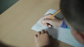 A cute little boy writing with a pencil close up. Clip. Little boy is writing with a pencil on paper