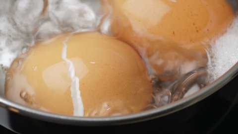 Chicken eggs boiling in stainless steel pan, closeup