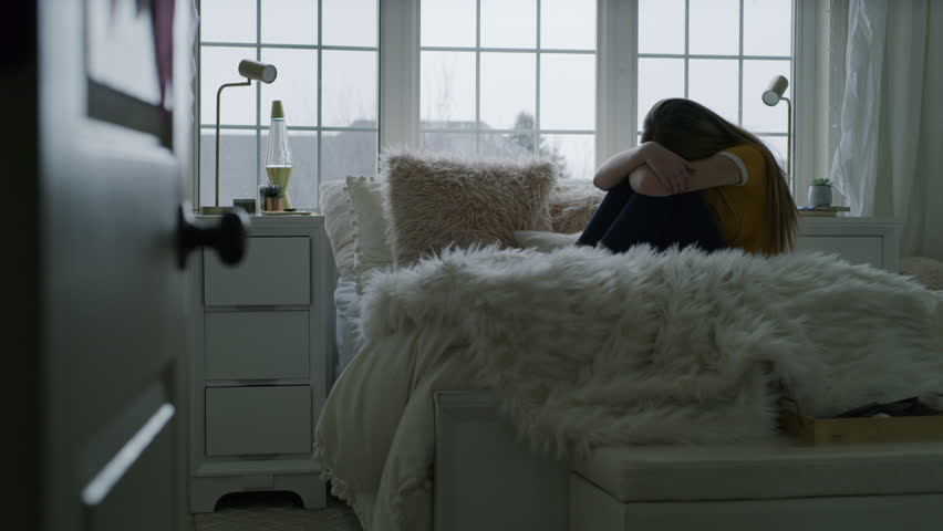 Sad girl sitting on bed in fetal position hiding face and rocking / Highland, Utah, United States