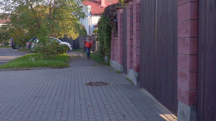 a ten year old student runs to, from the school with a backpack on his back and smiles. Slow motion
