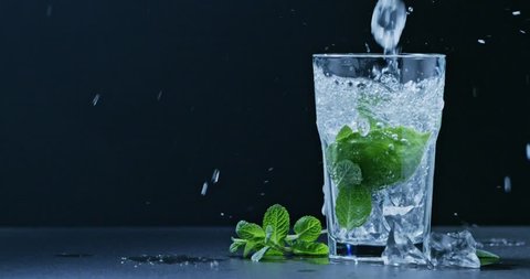 In a glass pour a cold drink with mint, lime and ice . Slow motion 2k video shooted on 240 fps