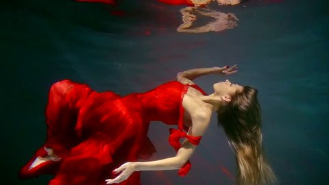 Attractive blonde woman floating underwater wearing beautiful red dress.