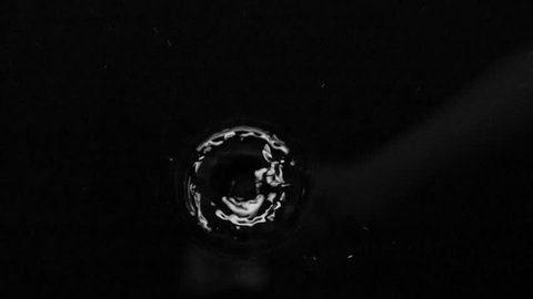Falling drop forms circles on the water surface. Black background. Slow motion