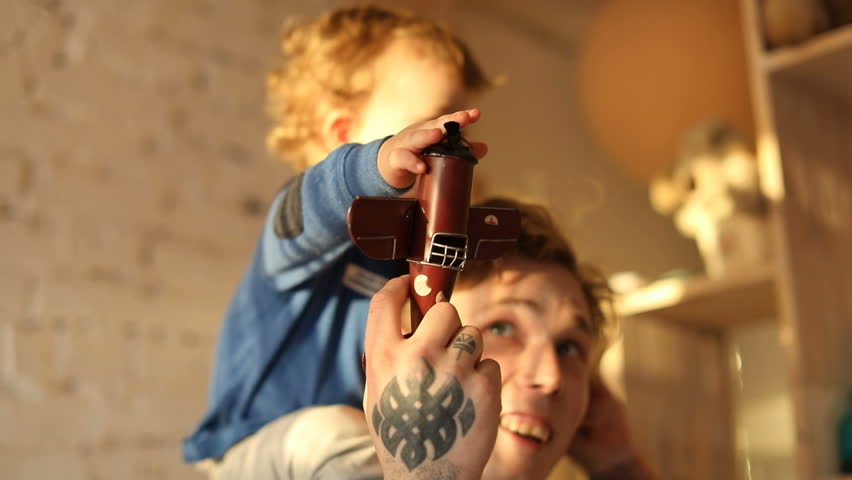 Cheerful man playing with little son showing retro toy while having fun at home.
