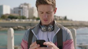 portrait of attractive young red head man using smartphone taking photo on sunny beachfront wearing headphones