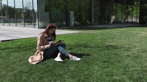 Young woman student using tablet outdoor sitting on grass and smiling.