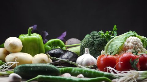 Fresh vegetables and chopped vegetables are on the rotating wooden table. Black background. Macro Shooting. 4K
