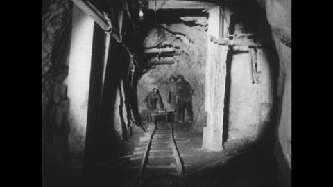 1950s: Light guides path through mine shaft as men in hardhats walk about doing various jobs.