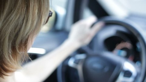 Young blond woman is learning driving, looking around, turning on turn signal