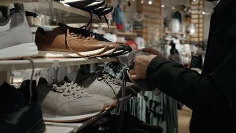 Young man buying summer shoes in a shoe store, student choose footwear sneakers in shopping mall