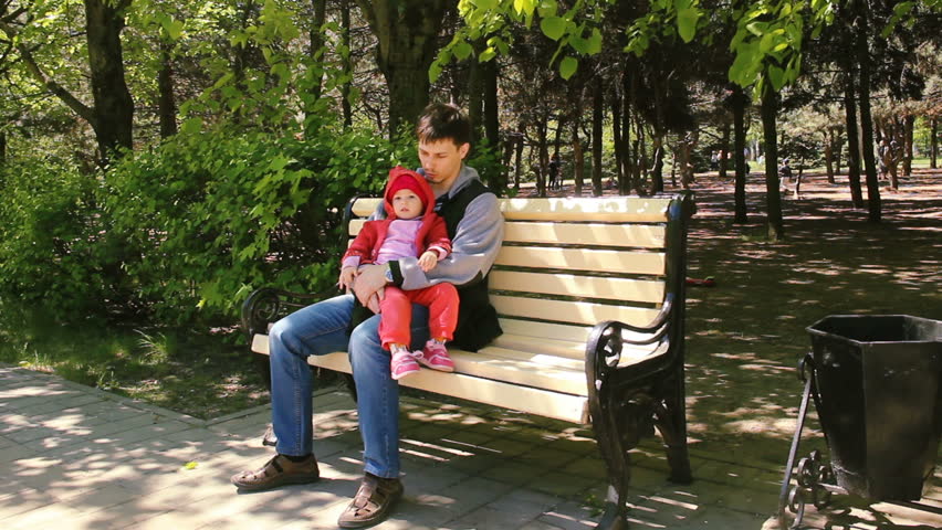 Dad is talking with his little daughter. A black-haired man with a short haircut and a little girl are sitting on a park bench. spring afternoon.