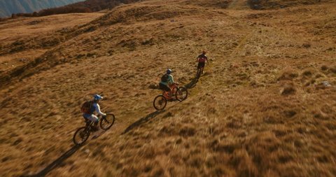 Aerial tracking shot of three mountain bikers cross-country riding to the top of the mountain with amazing peaks in the background.
