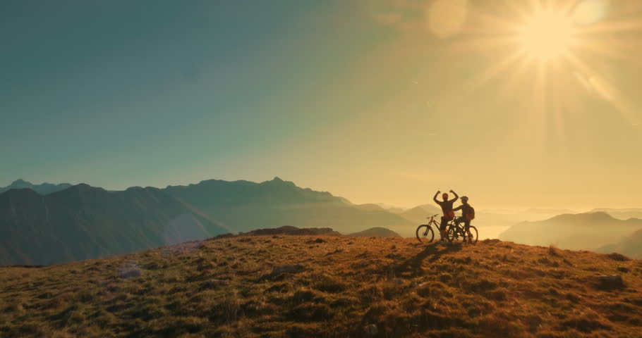 Aerial tracking wide shot of friends mountain biking in the sunset light with amazing peaks in background. | Shutterstock HD Video #1010578184