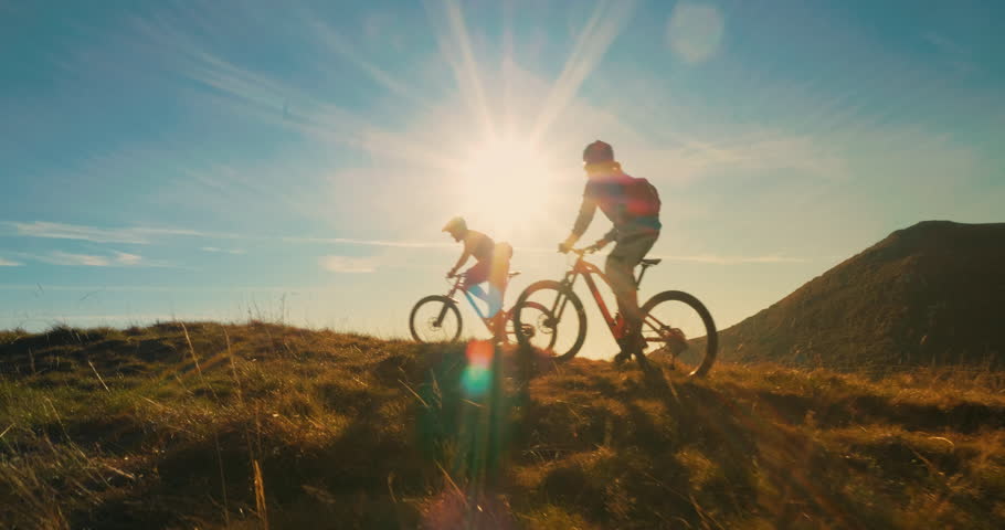 Two mountain bikers riding their bikes to the top in amazing sunlight. | Shutterstock HD Video #1010578247