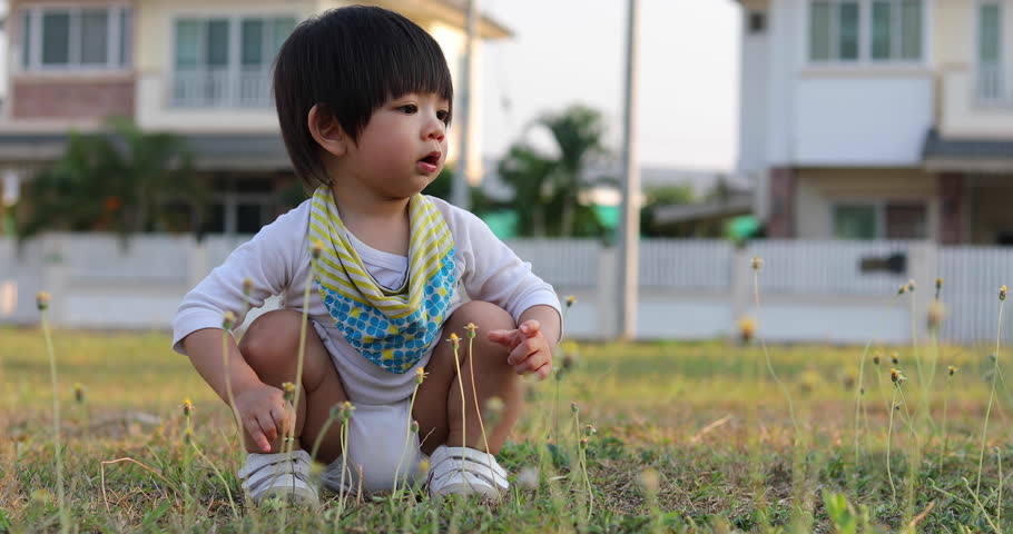 asian child playing flowers in lawn grass of village house with mom