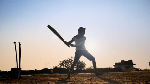 slow motion shot of young village teenager playing bare feet in a open field hits the cricket ball and runs. a silhouette shot of young man playing cricket in a summer vacation