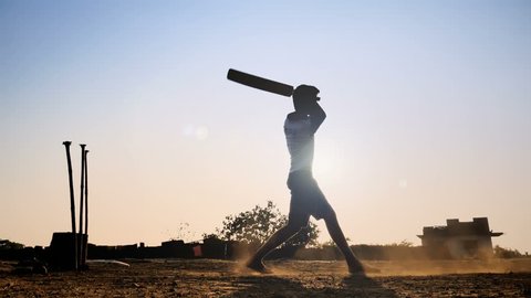 A slow motion shot of a young boy standing against the sun playing cricket match hits the ball for six . A silhouette shot a confident young man or batsman hits the cricket ball in the sky with bat. 