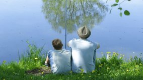 Happy family on summer vacations concept. Father and son fishing together at river bank. Real time full hd video footage.