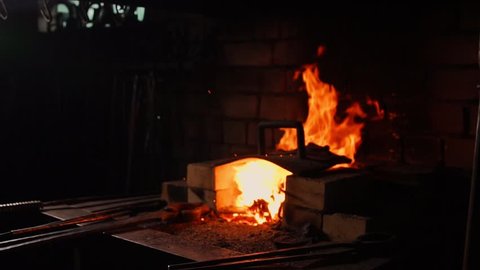 Closeup of a blacksmith fanning the flames of the furnace, using the tools prevents embers, sparks flying to the side in slow motion. Close-up of blacksmith's hand.