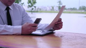 Business man working with mobile phone and document in public park with water pond background - business outdoor working concept