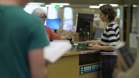 Students returning books to librarian in college library.