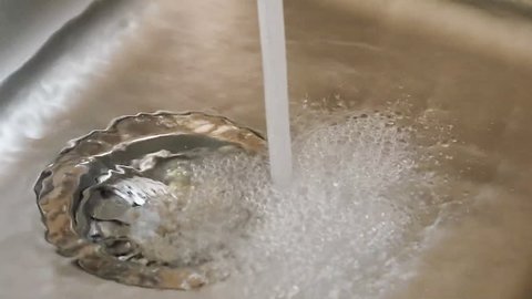 Water from a tap fills a kitchen sink.