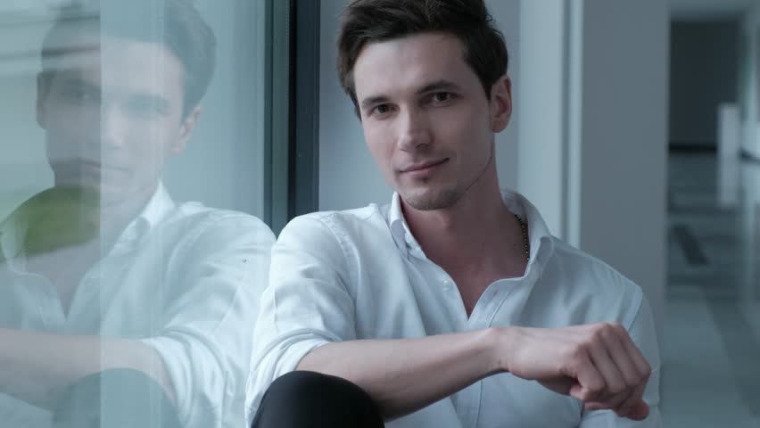 Portrait of a handsome man in a white shirt looking out the window.