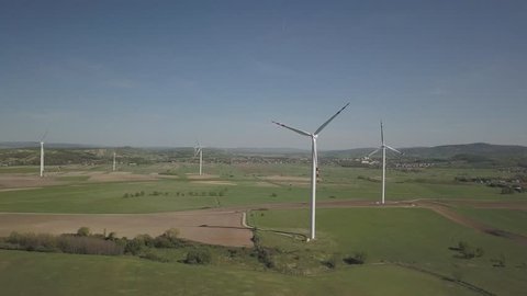 Flight near a wind power station in the daytime in the spring. Rotating blades of energy generators. Ecologically clean electricity. Modern technologies for the use of natural resources.