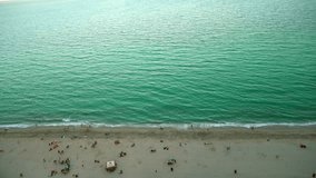 People rest on the beach. Tropical beach video loop showing footage with aerial bird eye view of green foaming ocean waves crushing against the coast line of Florida and overhead view of a tourists.