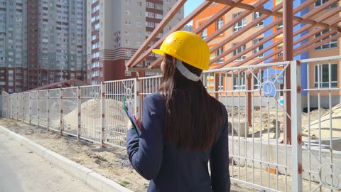 For 30 years, a young woman has been engaged in construction. business woman engineer in yellow helmet holds in hand a planet with papers and smiling. man on the background of the building under