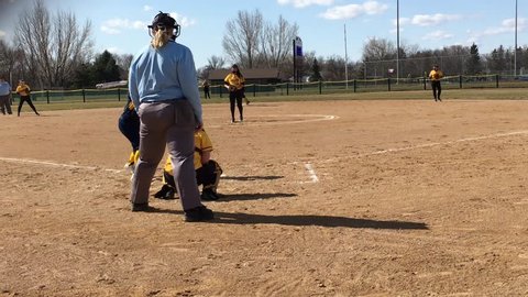 Fargo, ND - April 28, 2018:  Girls high school softball game from behind home plate with batter hitting ball and runners scoring thereafter.