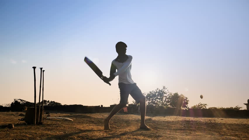 A young boy batting hits the cricket ball for a six in a open field in an Indian village. A slow motion shot of a teenager playing cricket against the sun strikes the cricket ball hard in rural India Royalty-Free Stock Footage #1010625815
