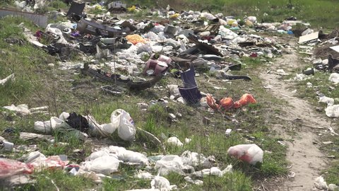 Elemental dump on the roadside near the outskirts of the city. Garbage is scattered on the green grass along the path. Pollution of the environment with plastic and other wastes