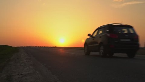 The car is driving along the road against the sunset.