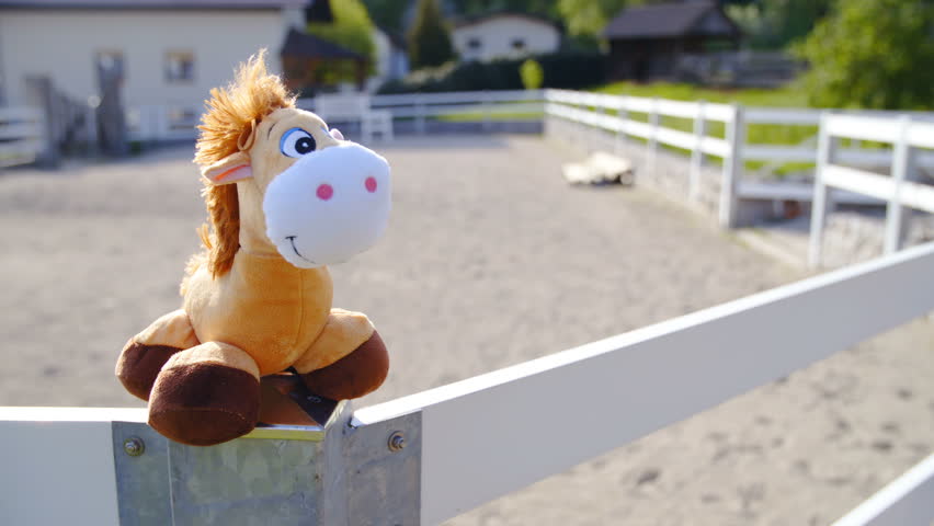 Horse mascot posing on riding arena fence 4K. Long shot dolly slide of horse toy on top of the fence standing in focus. Riding arena in background.
