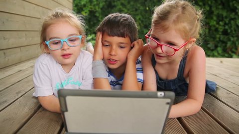 Children play on the tablet while lying on the wooden floor Stock Video