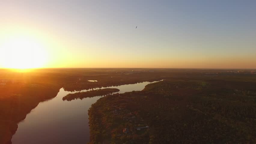 Flight down over the wooded coast of a large river next to a large city during sunset. Dnieper River, Ukraine. Back light.