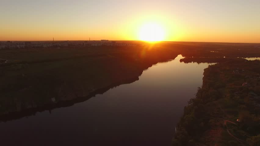 Flight over the wooded coast of a large river next to a city during sunset. Khortitsa Island, Dnieper River, Ukraine. Back light.