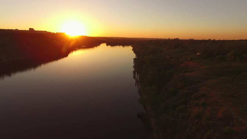 Flight over the rocky coast of a large river next to a city during sunset. Khortitsa Island, Dnieper River, Ukraine. Back light.