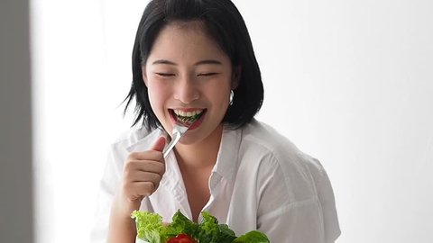 Asian woman eating fresh vegetables salad in her room.