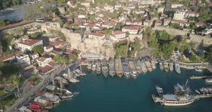 Low altitude aerial drone video Kaleici old town reverse to reveal ships in waterfront harbor and Mediterranean Sea in Antalya, Turkey. 4k at 23.97fps