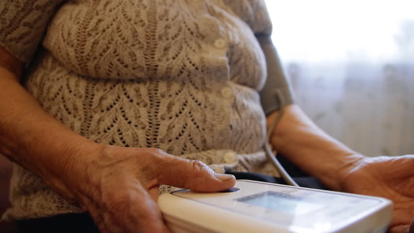 An old woman is measuring her blood pressure. Grandma