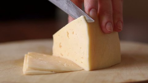 Close-up of female cook or housewife cutting cheese with a knife, slow motion.
