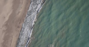 Forward bird's eye view aerial drone video waves breaking on sand beach from top down angle in Patara, Turkey. 4k at 23.97fps