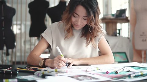 A young Asian woman working in a clothing store. A fashion designer makes outlines on paper.
